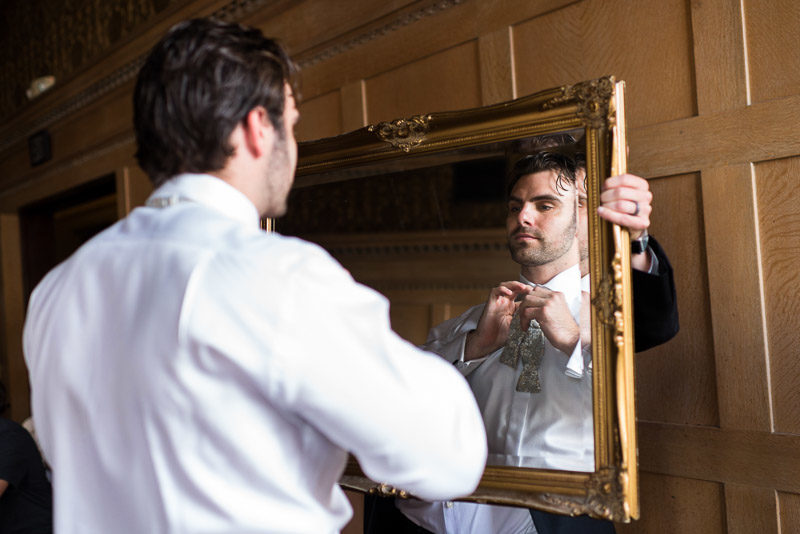 Groom putting on bowtie in mirror